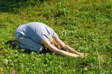 Kadın dışarıda yoga yapıyor, çimenlerde çocuk pozu veriyor (balasana)