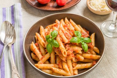 Makarna All 'Arrabbiata, domates soslu makarna, fesleğen ve parmesan peyniri ahşap masa üzerinde keten peçeteyle.