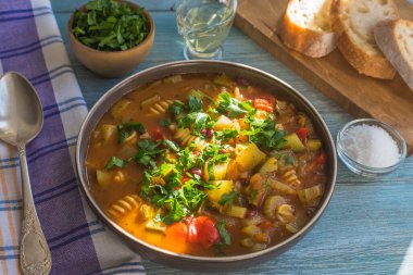 Geleneksel sebze çorbası, kırsal ahşap bir masada makarna ile servis edilir. Yakın plan, güneşli bir gün.