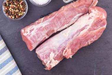 Koyu bir zemin üzerinde çiğ domuz filetosu ve yemek malzemeleri.