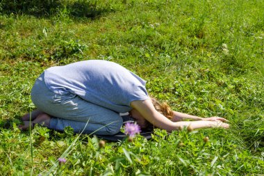 Kadın dışarıda yoga yapıyor, çimenlerde çocuk pozu veriyor (balasana)