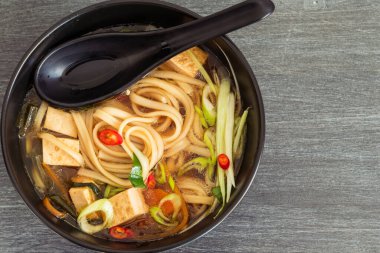 Vejetaryen diyet Asya çorbası udon erişteli, tofu ve sebzeli siyah kase, üst manzara, yakın plan, kopyalama alanı