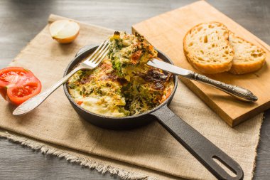 Geleneksel İtalyan omleti, brokoli ve domatesli, kırsal bir zeminde kızartma tavasında.