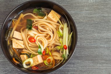 Vejetaryen diyet Asya çorbası udon erişteli, tofu ve sebzeli siyah kase, üst manzara, yakın plan, kopyalama alanı