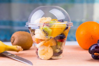 Tasty fruit and berry salad in a plastic cup on a wooden table - a vegetarian breakfast clipart