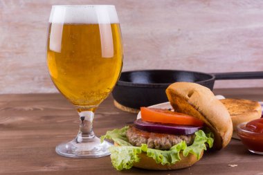 Ev yapımı hamburger, ızgara et, soğan ve bir bardak birayla birlikte koyu ahşap arka planda fotokopi alanı ile birlikte.