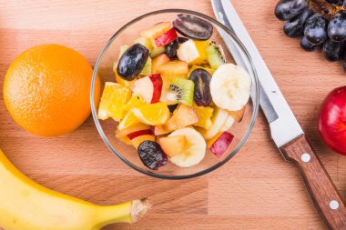 Tahtada meyve salatası ve malzemelerle dolu cam kase. Üst manzara, düşük kalorili diyet kavramı.