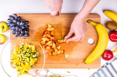 Ahşap kesim tahtasında meyve salatası için erik kesen kadın.
