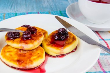Kiraz reçelli leziz peynirli krepler, ahşap bir arka planda meyve çayıyla.