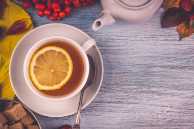 Bir fincan limonlu çay eski ahşap masanın üzerinde sonbaharın kırsal yaprakları, metal bir fincanda kamış şeker küpleri. Boşluğu kopyala