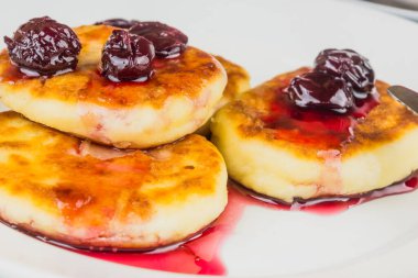 Beyaz tabakta kiraz reçelli Rus peynirli kekleri.