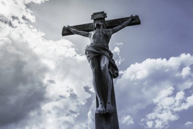 Antik haç, güneş tarafından aydınlatılmış, bulutlarla kaplı gökyüzüne karşı.