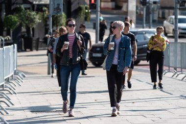 Moskova, Rusya, 14 Temmuz 2019 - İki genç kadın yürür, kağıt bardaklardan kahve içer ve konuşurlar