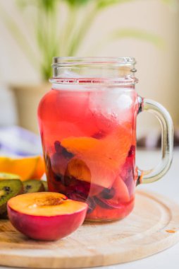 Bardakta buzlu kırmızı meyve çayı ve tahta tepside taze tropikal meyveler.