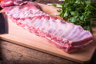 Tahta üzerinde taze domuz pirzolası, taze kişniş ve yeşil soğan.