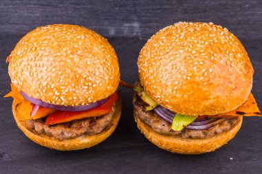 Koyu arkaplanda iki ev yapımı hamburger ve fırında sebze.