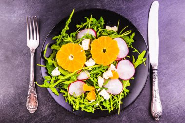Vejetaryen salatası, roka, turp, mandalina ve keçi peyniri tabakta.