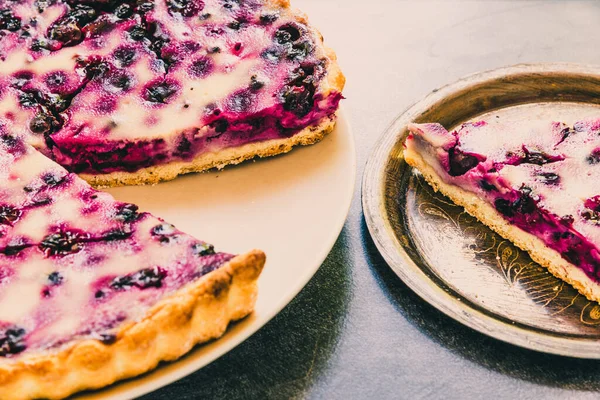 Sliced homemade tart with berries of black currant on a dark background