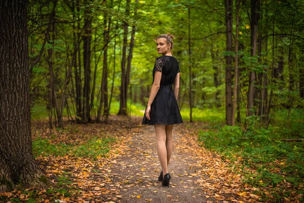 秋の森の小道に黒いドレスを着た美しい若い女性 — ストック写真