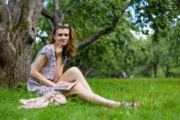 若いかわいい女性は本を読んで 木の下の庭に座って — ストック写真