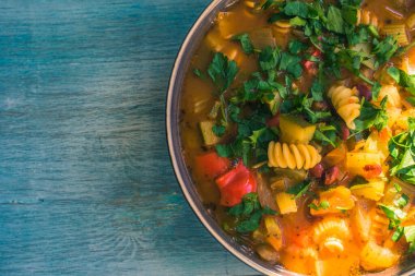 Geleneksel sebze çorbası makarna ve doğranmış yeşil maydanoz kırsal ahşap masa manzaralı bir tabakta yakın plan, bir tarif için yer kopyalama