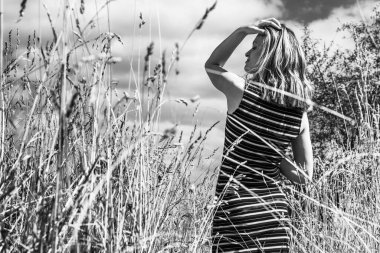 Güzel bir genç kadın kuru bir çimenlikte bulutlu bir gökyüzüne karşı - siyah ve beyaz bir fotoğraf