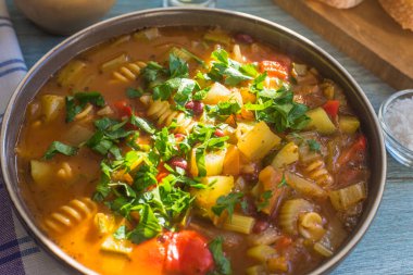 Geleneksel sebze çorbası, kırsal ahşap bir masada makarna ile servis edilir. Yakın plan, güneşli bir gün.