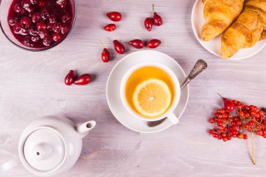 Limonlu çay, çaydanlık, sonbahar meyvelerinden reçel ve kruvasan, ahşap bir arka planda.