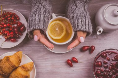 Sıcak kazaklı bir kadın limonlu bir fincan çay tutuyor.