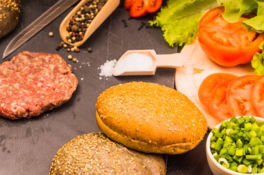 Çiğ hamburger, çörek, domatesli salata ve ev yapımı hamburger malzemeleri.