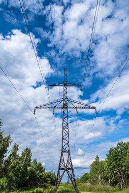 Gökyüzüne karşı kırsal kesimde bulutlar olan yüksek voltajlı bir elektrik hattı kulesi.