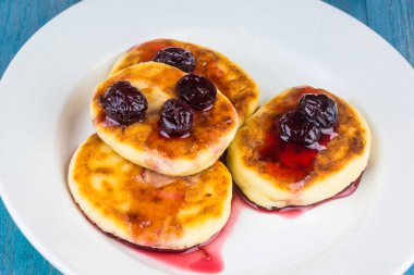 Beyaz tabakta kiraz reçelli Rus peynirli kekleri.