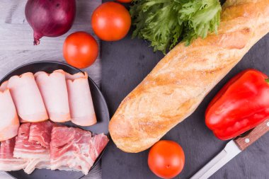 Sandviç için baget ve malzemeler. Domates, pastırma, soğan, marul, füme domuz eti.