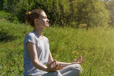 Genç çekici kadın dışarıda Lotus pozisyonunda meditasyon yapıyor.