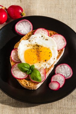 Yağda yumurta ve siyah tabakta turplu lezzetli bir sandviç.