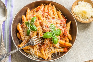 Makarna All 'Arrabbiata, domates soslu makarna, fesleğen ve parmesan peyniri ahşap masa üzerinde keten peçeteyle.