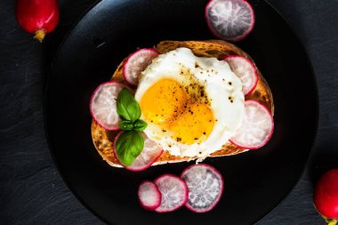 Yağda yumurta ve siyah tabakta turplu lezzetli bir sandviç.