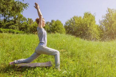 Güneşli bir günde, dışarıda yoga yapan çekici bir kadın Virabhadrasana, savaşçı pozu.