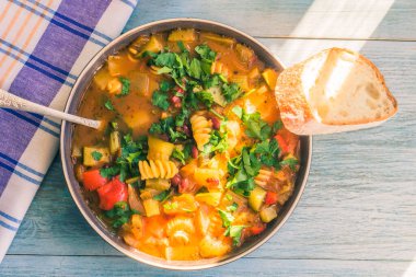 Geleneksel sebze çorbası makarna ve doğranmış yeşil maydanoz kırsal ahşap bir masa üzerinde peçeteyle yakın plan, güneşli bir gün - üst manzara, bir tarif için kopyalama alanı