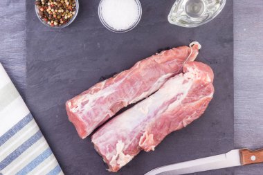 Koyu bir zemin üzerinde çiğ domuz filetosu ve yemek malzemeleri.