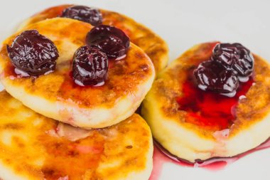 Beyaz tabakta kiraz reçelli Rus peynirli kekleri.