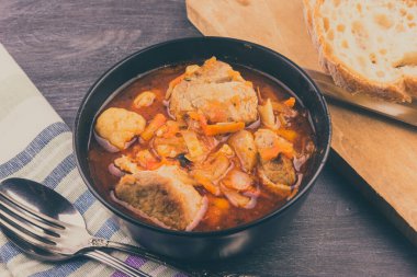 Siyah kasede sebzeli haşlanmış domuz eti ve kırsal bir masada bir parça ekmek.