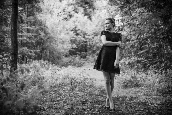 Attractive stylish young woman in a black dress in the forest