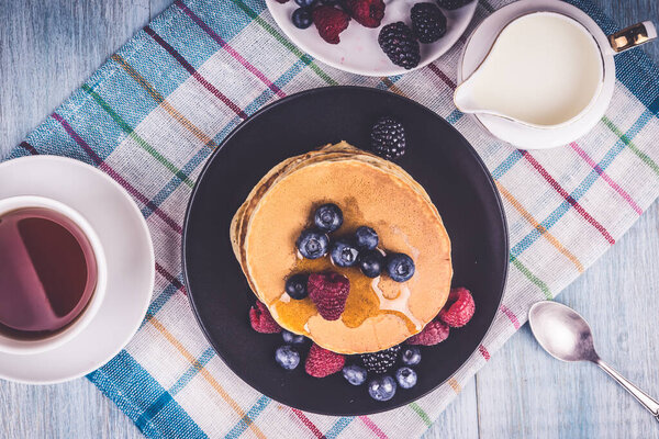 Pancakes with maple syrup and berries and tea on a wooden rustic table - top view