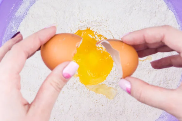 woman prepares dough from flour and eggs, female hands break the egg