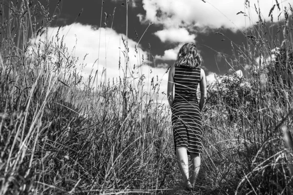 雲と空に対して乾燥した芝生のフィールドで美しい若い女性 黒と白の写真 — ストック写真