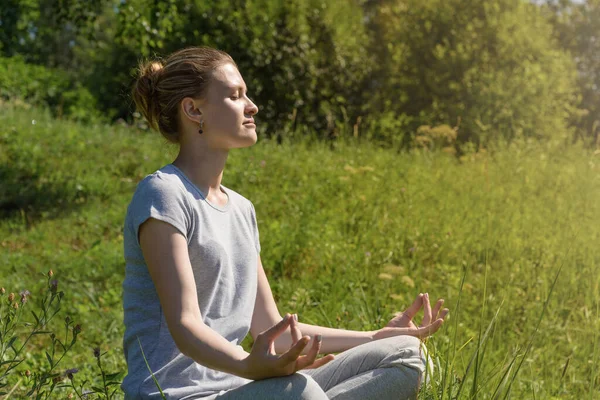 Genç çekici kadın dışarıda Lotus pozisyonunda meditasyon yapıyor.
