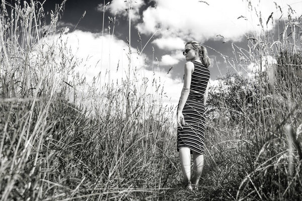 Beautiful young woman in a dry grass field against a sky with clouds - black and white photo