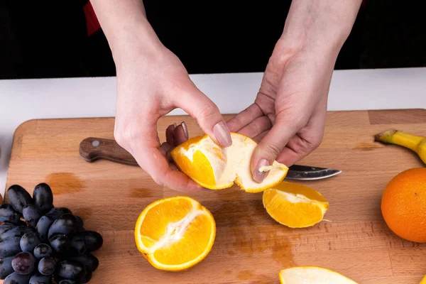 Woman peeling orange with fruit salad on a wooden cutting board - female hands, healthy eating concept