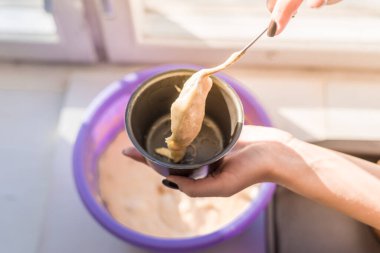 Kadın kaşıkla kek kalıbına hamur koyuyor.